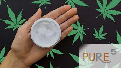 a hand holding a cream with cbd in it extracted from marijuana plant