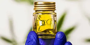 a jar with cannabidiol oil in a hand with blue gloves